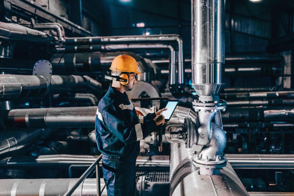 Jeune homme en tenue de travail utilisant une tablette dans une usine de chauffage.